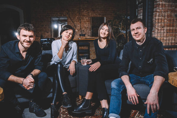 Веселые парни и девочки сидят на диване и улыбаются, глядя в камеру. Место для текста или рекламы.