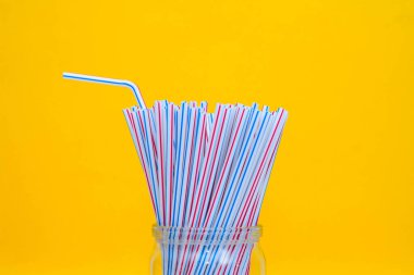 Sarı arka planlı cam bir kavanozda plastik pipetler. Metin için boşluk.