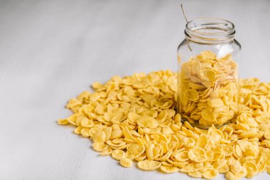 Beyaz ahşap yüzeyde cam bir kavanozda mısır gevreği. Metnin için yer.