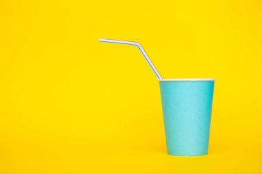 Sarı arka planda renkli plastik pipetler içen mavi kağıt bardaklar. Partiye hazırız. Minimalist stil. Kopyala, metin için boşluk.