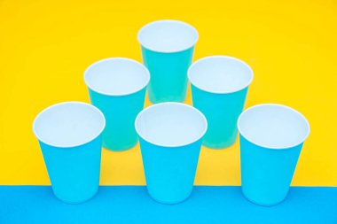 Sarı arka planda tek kullanımlık mavi bardaklar piramidi. Partiye hazırız. Kopyala, metin için boşluk.