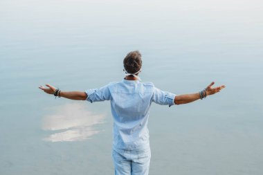 Yakışıklı adam ahşap köprüde duruyor ve mavi gökyüzünün su refleksine bakıyor ellerini yana atıyor. Arkadan ateş et. Özgürlük rahatlama kavramı. Metin veya reklam için yer.