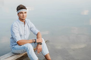 Adam ahşap köprüde oturuyor ve mavi gökyüzünün su refleksine bakıyor. Özgürlük rahatlama kavramı. Metin veya reklam için yer.