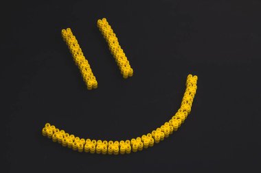 Sarı renkli renkli plastik tuğlalar, siyah arka planda bir gülümseme oluşturuyor. Oyuncaklar için küçük, parlak yedek parçalar. Üst görünüm