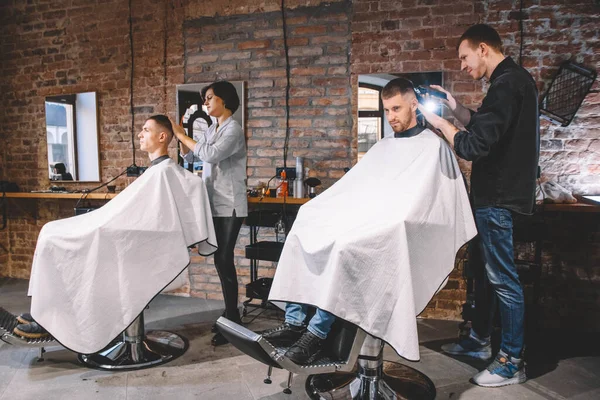 Los peluqueros cortan a sus clientes en la peluquería. Concepto de publicidad y peluquería — Foto de Stock