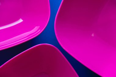 Mavi arka planda bir dizi pembe plaka. Mutfak için plastik aletler. Üst Manzara. Minimalist stil. Kopyala, metin için boşluk.