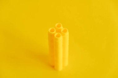 Sarı arka planda bir kule şeklinde sarı plastik yapı taşları. Plastik yapı taşlarının arka planı. Oyuncaklar için küçük, parlak yedek parçalar. Kopyala, metin için boşluk.