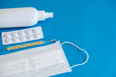 Tıbbi tek kullanımlık maske, antiseptik, haplar ve mavi arka planda civa termometresi. Tıbbi hijyen ve virüs koruma kavramı. Üst Manzara. Kopyala, metin için boşluk.