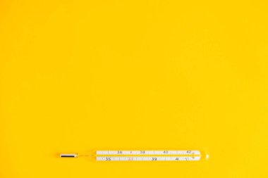 Sarı arka planda tıbbi cıva termometresi. Üst Manzara. Kopyala, metin için boşluk.