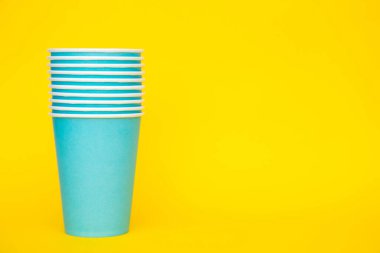 Sarı arka planda tek kullanımlık mavi bardaklar. Partiye hazırız. Kopyala, metin için boşluk.