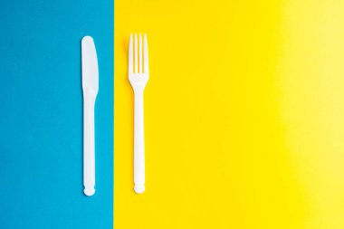 Sarı ve mavi arka planda plastik beyaz çatal ve bıçak. Mutfak aletleri. Üst Manzara. Minimalist stil. Kopyala, metin için boşluk.