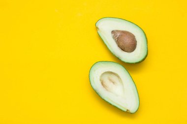 Sarı arka planda iki yarım avokado. Üst Manzara. Kopyala, metin için boşluk.