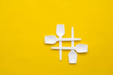 Sarı arka planda beyaz plastik kaşıklar. Fast food, eko ve plastik konsept yok. Üst Manzara. Kopyala, metin için boşluk.