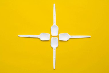 Sarı arka planda beyaz plastik kaşıklar. Fast food, eko ve plastik konsept yok. Üst Manzara. Kopyala, metin için boşluk.