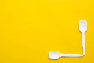 Sarı arka planda beyaz plastik kaşıklar. Fast food, eko ve plastik konsept yok. Üst Manzara. Kopyala, metin için boşluk.
