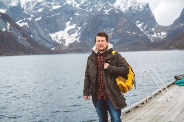 Sırt çantalı bir gezgin, karlı dağların ve gölün arka planında, ahşap bir iskelede duruyor. Metin veya reklam için yer.