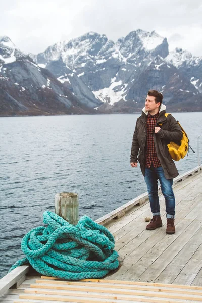 Traveler man with a backpack standing on a wooden pier the background of snowy mountains and lake. Place for text or advertising.