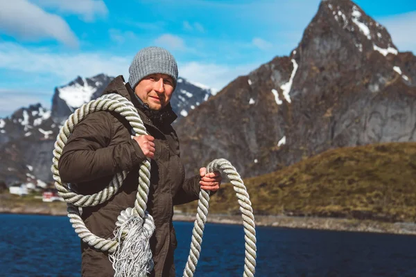 Brutal man with a rope on his shoulder against the background of the mountains and the blue sky. Copy space. Can use as banner.