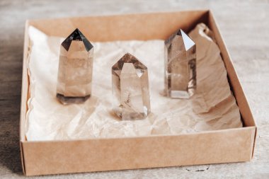 Three smoky natural quartz crystals in a kraft paper box on wooden background. Copy, empty space for text. clipart
