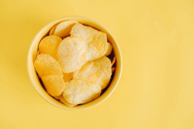 Sarı arka planda sarı bir kasede patates cipsi. Üst Manzara. Kopyala, metin için boşluk.
