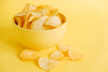 Sarı arka planda sarı bir kasede patates cipsi. Kopyala, metin için boşluk.