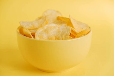 Sarı arka planda sarı bir kasede patates cipsi. Kopyala, metin için boşluk.