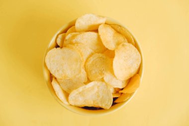 Sarı arka planda sarı bir kasede patates cipsi. Üst Manzara. Kopyala, metin için boşluk.