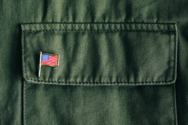 USA flag pin badge on green jacket pocket. Top view. Copy, empty space for text.