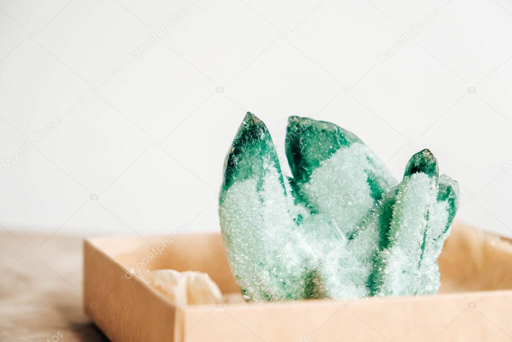 Raw emerald and gemstone rough rock crystal in a kraft paper box on wooden background. Copy, empty space for text.