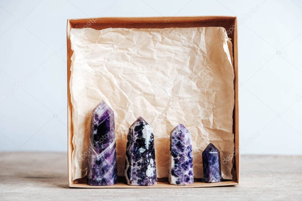 Amethyst polished crystal point in a kraft paper box on wooden background. Copy, empty space for text.