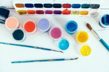 Beyaz ahşap masaya boyamak için renkli gouache boyaları ve fırçalar. Üst Manzara. Kopyala, metin için boşluk.