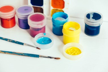 Beyaz ahşap masaya boyamak için renkli gouache boyaları ve fırçalar. Kopyala, metin için boşluk.