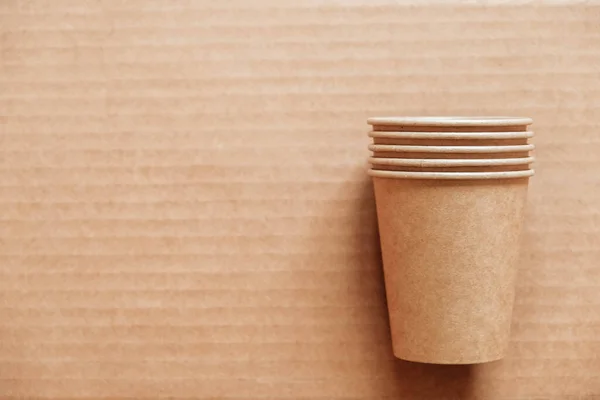 Disposable paper cups on kraft paper background. Eco friendly disposable tableware. Zero waste concept. Top view. Copy, empty space for text.