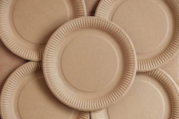 Disposable paper plates on kraft paper background. Eco friendly disposable tableware. Top view. Copy, empty space for text.