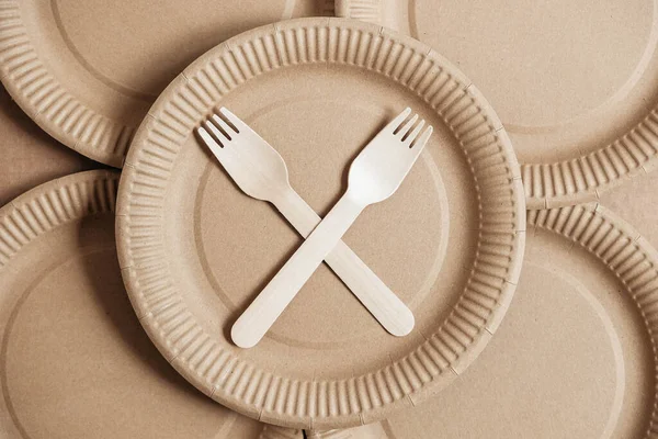 Wooden forks and plates on kraft paper background. Eco friendly disposable tableware. Also used in fast food, restaurants, takeaways, picnics. Top view. Copy, empty space for text.