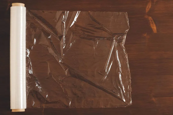 Big roll of transparent packaging film on a wooden background. Top view. Copy, empty space for text.