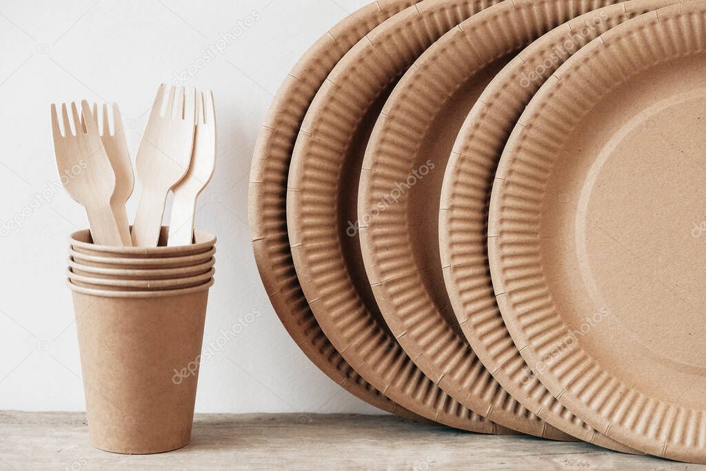 Wooden forks and paper cups with plates on wooden background. Eco friendly disposable tableware. Also used in fast food, restaurants, takeaways, picnics. Copy, empty space for text.