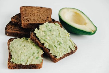 Beyaz ahşap bir masada avokado ile kahverengi ekmek dilimleri. Kopyala, metin için boşluk.