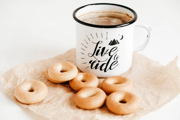 Metal mug with hot drink and mini round bagels on a white wooden background. Copy, empty space for text.