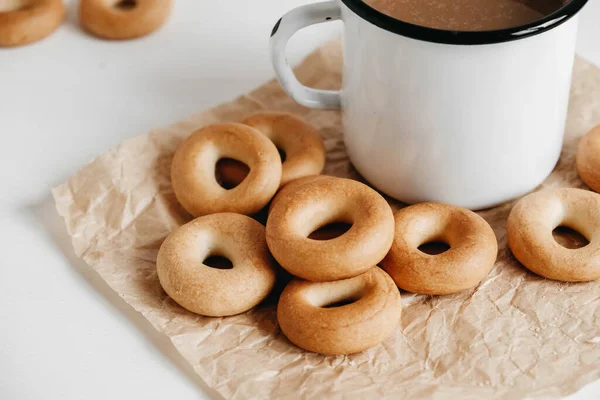 Metal mug with hot drink and mini round bagels on a white wooden background. Copy, empty space for text.