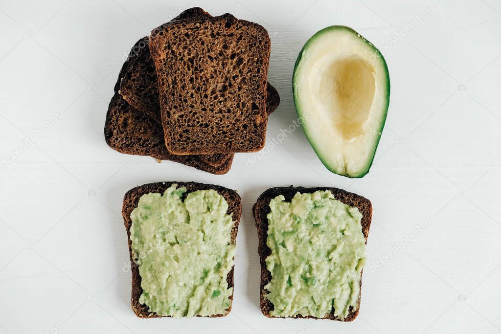 Slices of brown bread with avocado on a white wooden table. Top view. Copy, empty space for text.