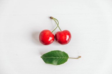 Beyaz ahşap arka planda yeşil yapraklı taze kirazlar. Üst Manzara. Kopyala, metin için boşluk.