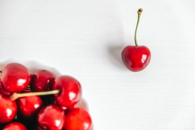 Beyaz ahşap zemin üzerinde beyaz bir tabakta taze kırmızı kirazlar. Üst Manzara. Kopyala, metin için boşluk.