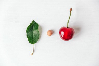 Beyaz ahşap arka planda yeşil yapraklı taze kiraz. Üst Manzara. Kopyala, metin için boşluk.