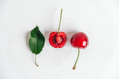 Beyaz ahşap arka planda yeşil yapraklı taze kirazlar. Üst Manzara. Kopyala, metin için boşluk.