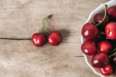 Tahta zemin üzerinde beyaz bir tabakta taze olgun kirazlar. Üst Manzara. Kopyala, metin için boşluk.