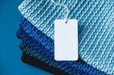 Lacivert, açık mavi ve gri renkli ipliklerden örülmüş kumaş yığını. Mavi arka planda boş etiket var. Üst Manzara. Kopyala, metin için boşluk.