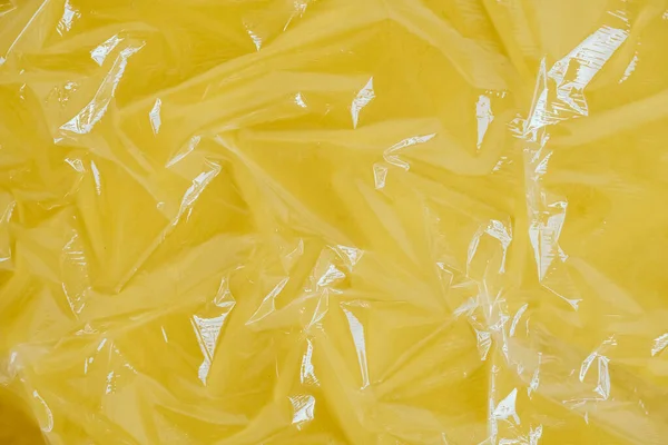 Wrinkled transparent plastic texture on an yellow background. Transparent cellophane texture on an yellow backing. Top view. Copy, empty space for text.