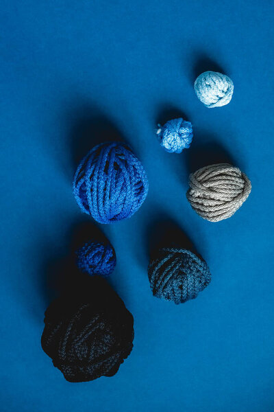 Balls of threads of dark blue, light blue, gray colors on a blue background. Top view. Copy, empty space for text.