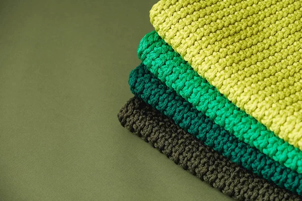 Stack of knitted material from threads of yellow, green, brown colors on a green background. Copy, empty space for text.